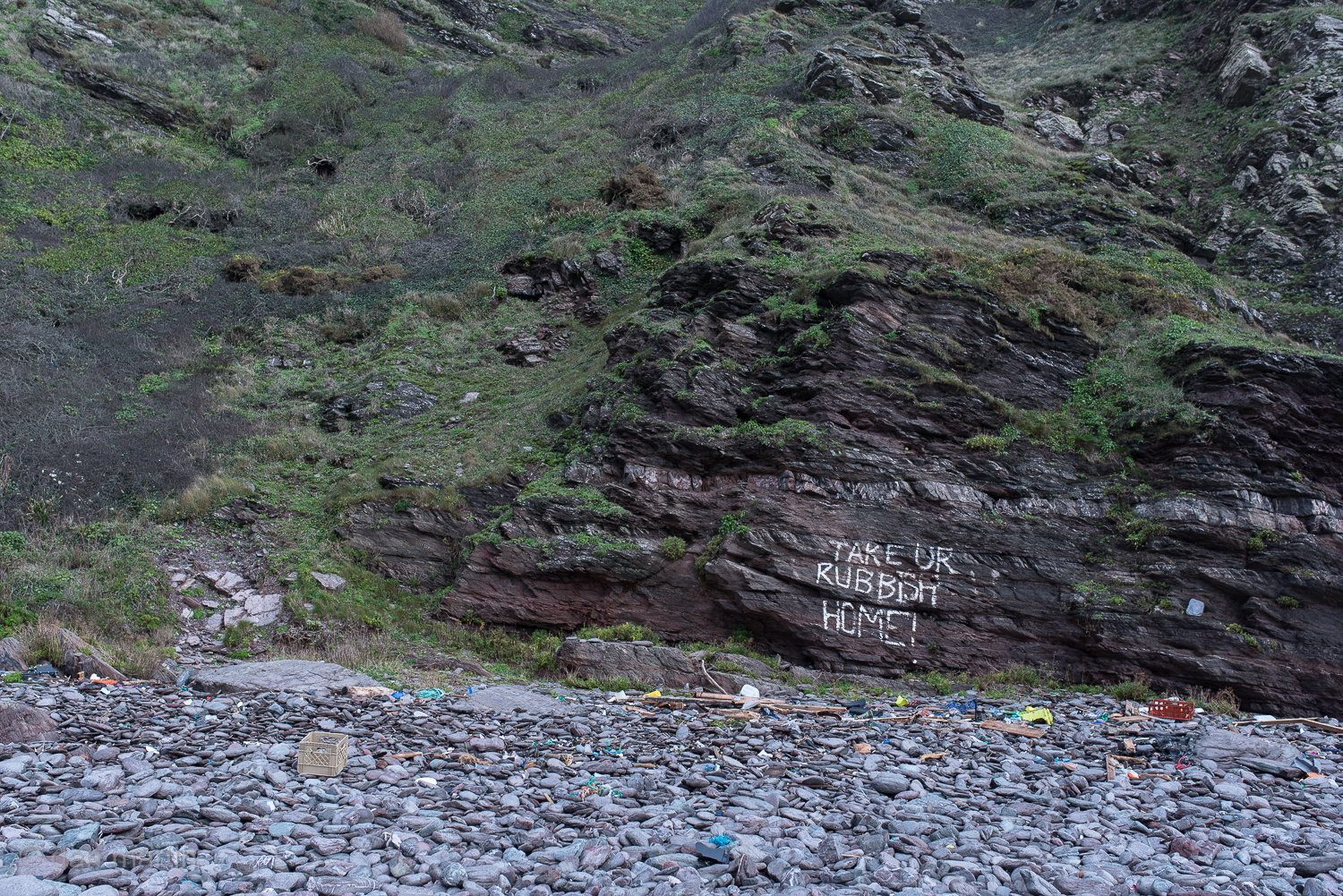 The irony; graffiti scrawled upon raw rock.  Litter spewed up by the sea, mans waste, below. 