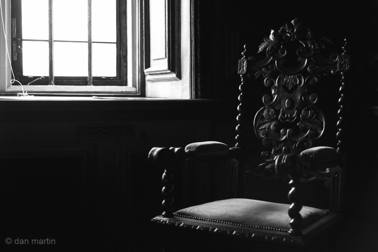 The chair caught in the light, illuminating the carved wood frame and details. Somewhat solemn. Awaiting.