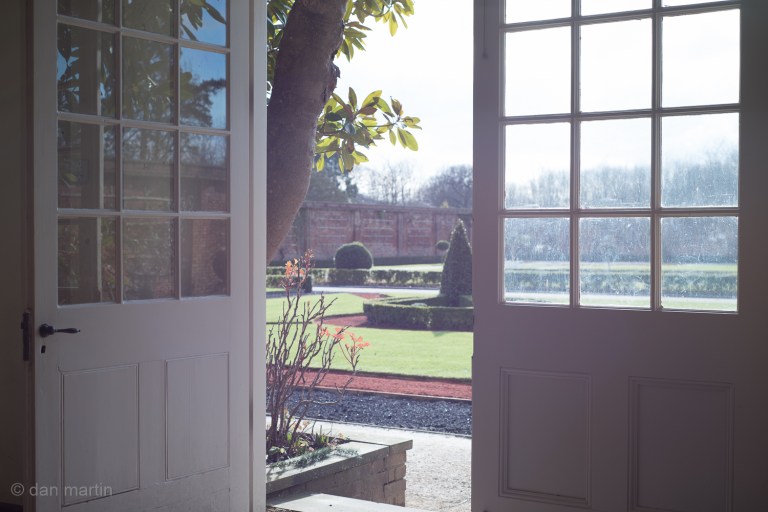 Orangery; full of sun. Bright light seeping in. The warmth that goes with.  Looking out. Lens flare be damned. 